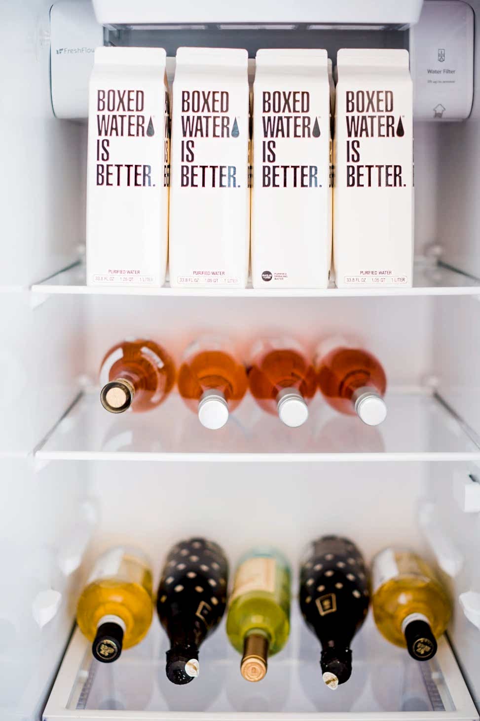 The inside of a fridge stocked with boxed water, rose, white wine, and sparkling wine