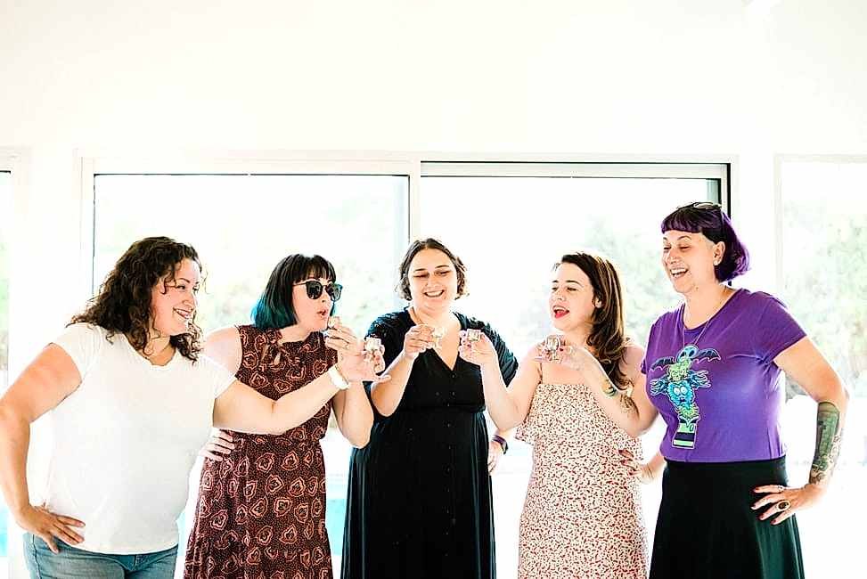 five women toasting shots in mini goblets in front of a window
