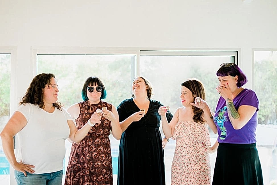 five women making faces after taking shots from mini goblets, in front of a window