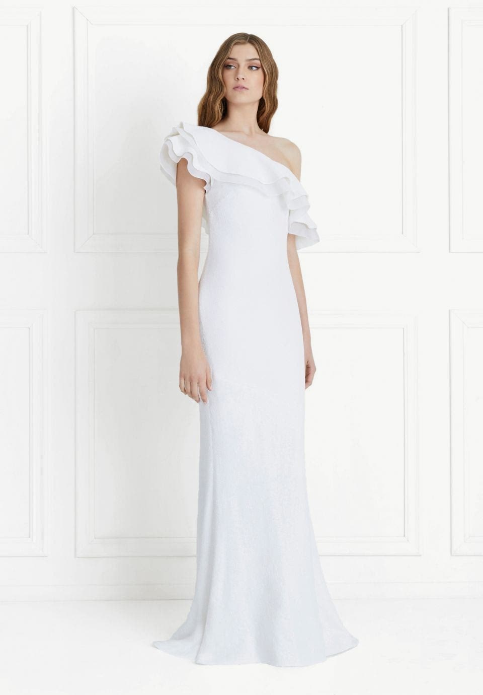 A woman wears a white dress with an asymmetrical ruffle neck