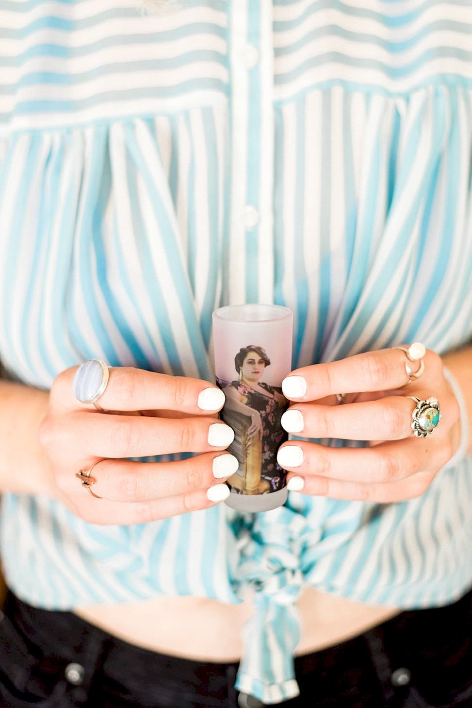 A woman in a blue and white striped tied blouse holds a frosted shotglass with a photo of a woman printed on it