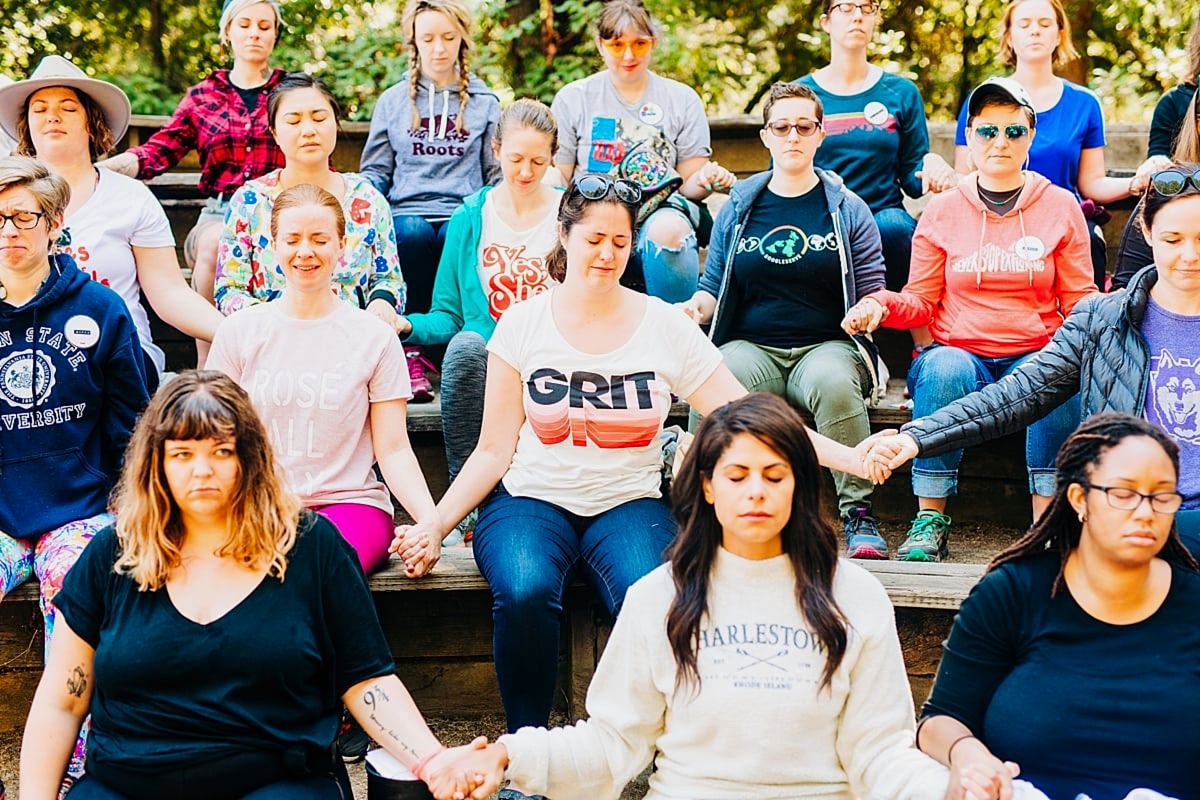women sitting with eyes closed, holding hands, with serious and emotional expressions at the compact summer camp in la Honda, CA
