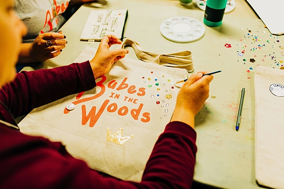 A woman bedazzling a Babes in the Woods tote bag at the compact summer camp in la Honda, CA