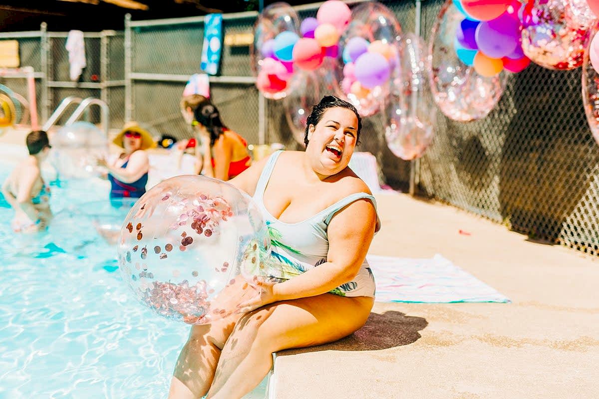 A woman sitting poolside, laughing, holding a glittery beach ball at the compact summer camp in la Honda, CA