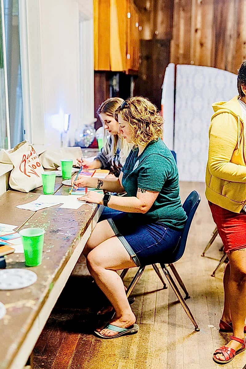 Women watercoloring in a wood-paneled roomat the compact summer camp in la Honda, CA