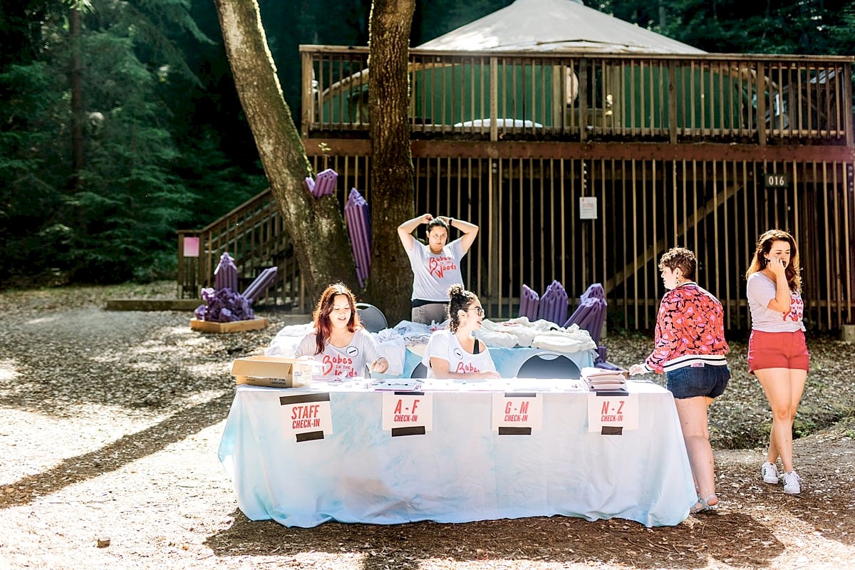 Women getting ready to check in and greet campers at a check-in table in front of a yurt at the compact summer camp in la Honda, CA