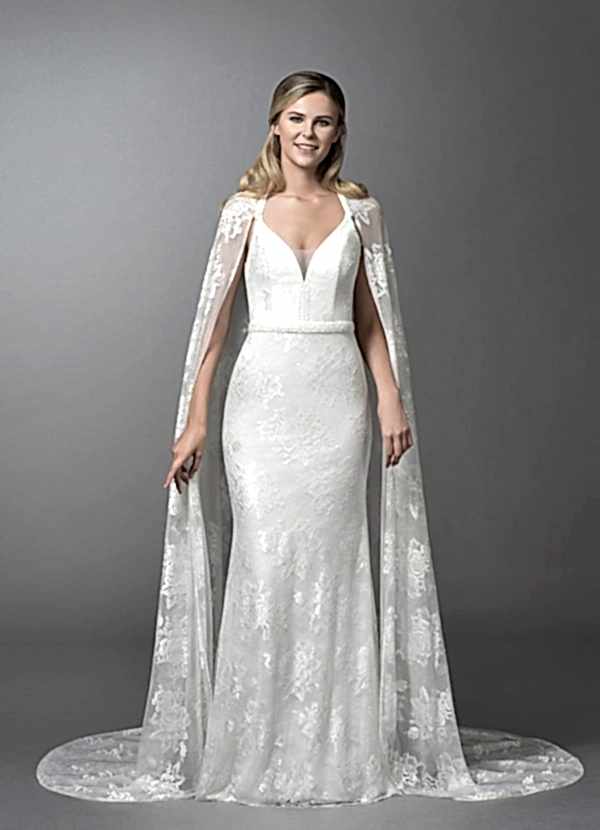 Smiling blonde woman wearing white gown and cape in grey room