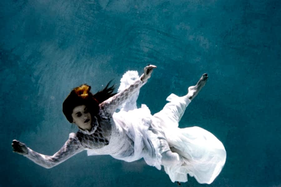 A red-headed woman in a wedding dress, floating, submerged in a blue swimming pool