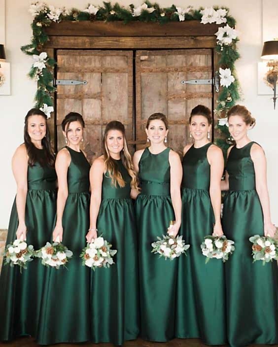 Group of women wearing winter wedding colors: dark green dresses and holding bouquets with greenery, white flowers, and pinecones