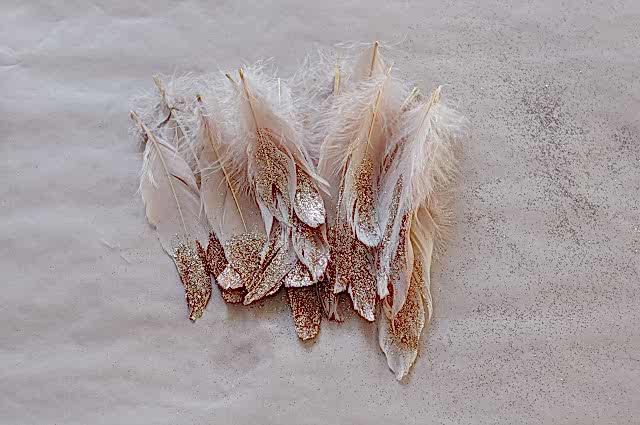 Pile of feathers in winter wedding colors: white and cream feathers dipped in gold glitter