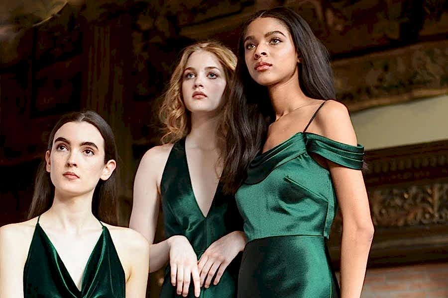 Three women wearing dark green dresses and holding flowers