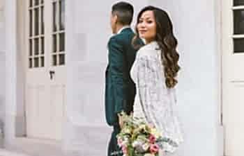 Brunette woman and man walking away, with woman in white cape and dress and holding bouquet