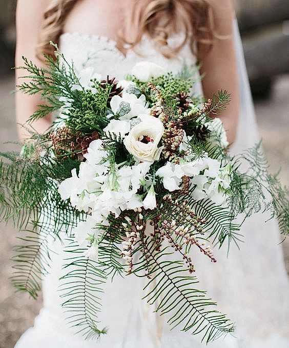 woman in white dress holding bouquet with fir sprigs