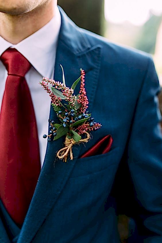 Close up of man in winter wedding colors: a medium blue coat with a dark red tie and coordinating boutonnière
