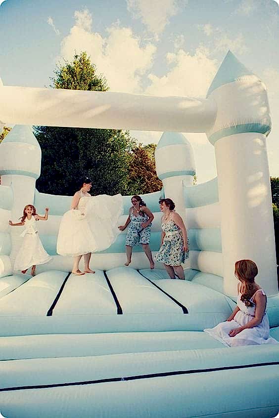 wedding ideas for a bride and bridal party jumping in a light blue and white bouncy castle
