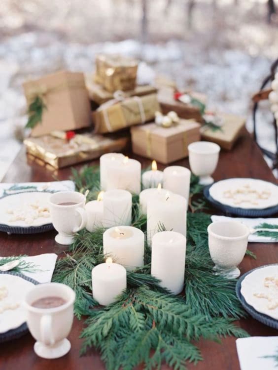 tablescape in winter wedding colors: white candle and fir table runner among dishes with blue accents and a pile of gold and kraft-wrapped gifts