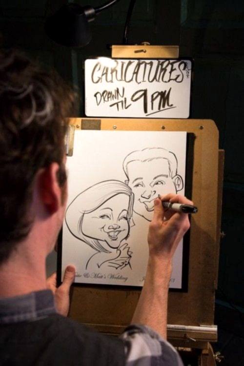 Wedding ideas for activities—a man drawing a caricature beneath a sign that reads "Caricatures drawn til 9pm"