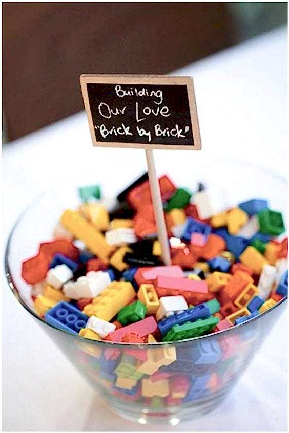wedding ideas for activities—legos in a glass bowl on a table with a sign that reads "Building our love brick by brick" 