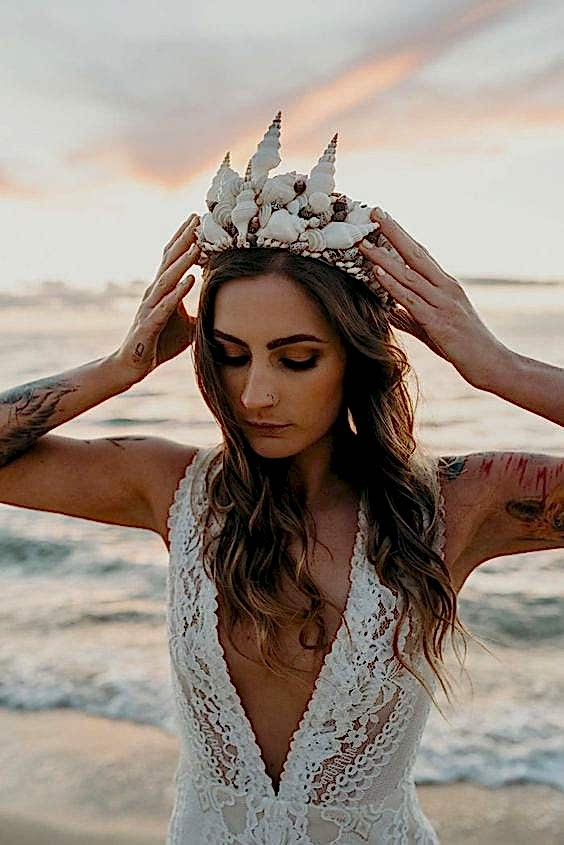 wedding ideas for headpiece—woman wearing a shell crown in a wedding dress with waves crashing behind her as the sun sets