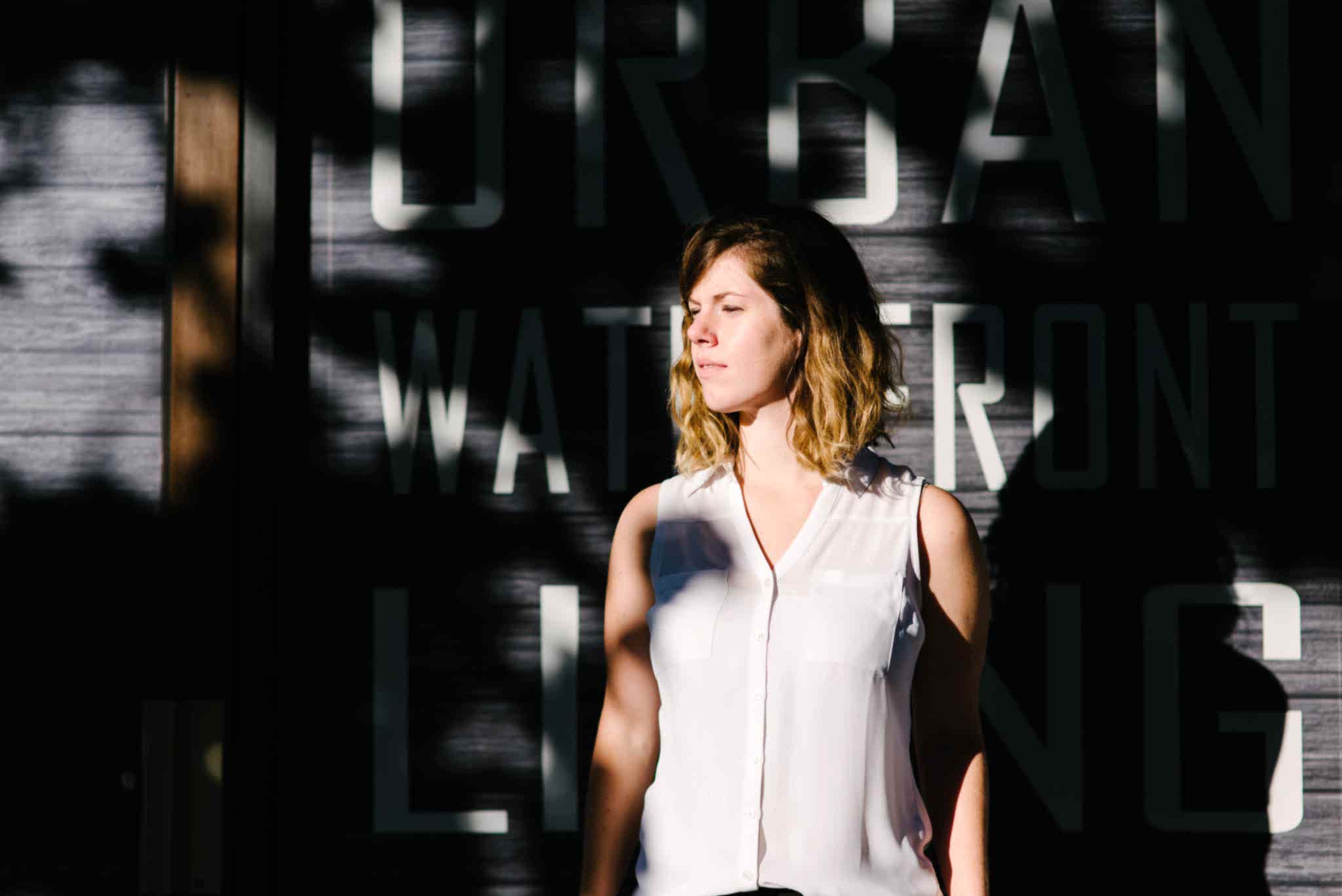 A woman stands against a wall full of shadows