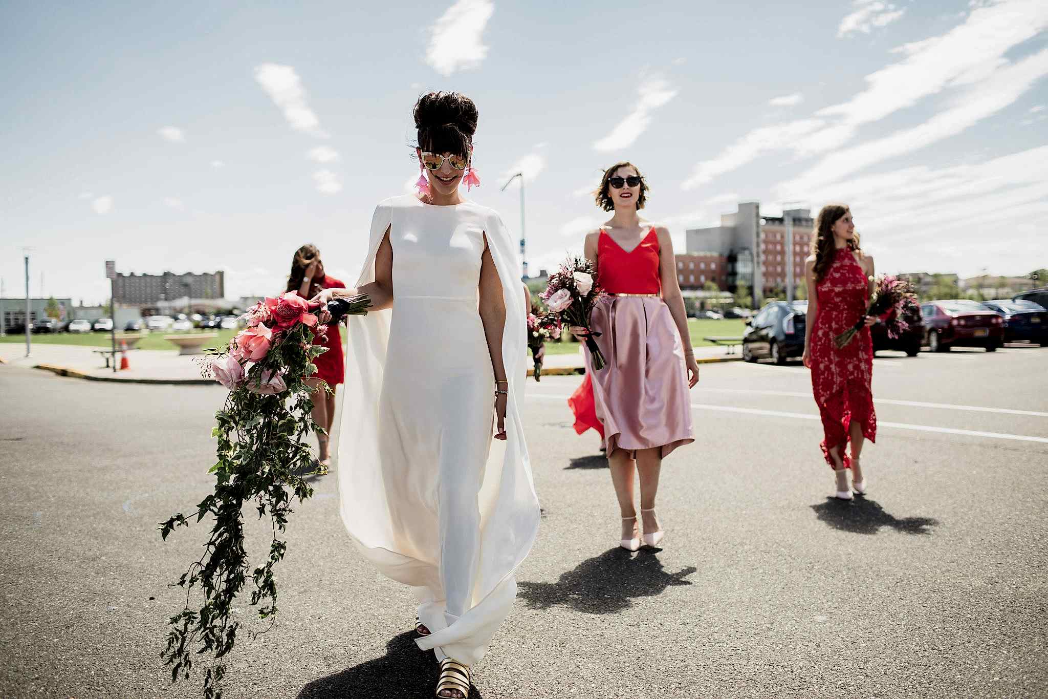 bride wearing a wedding dress with a cape and cascading bouquet with bridesmaids in mismatched hot pink and red dresses