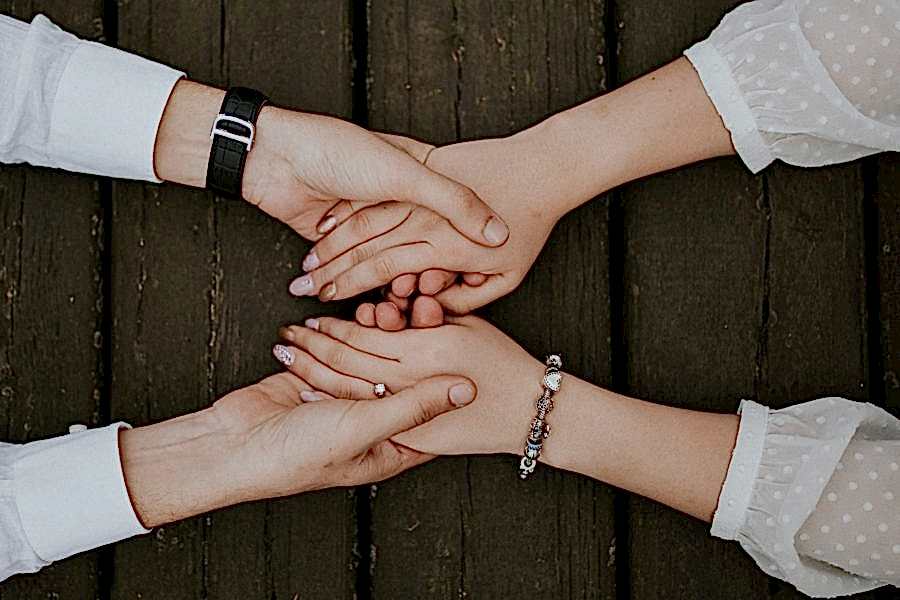 Two people's hands, holding each other over a wooden table.
