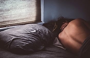 A person lies in bed, huddled in corner, back to you, next to an empty pillow