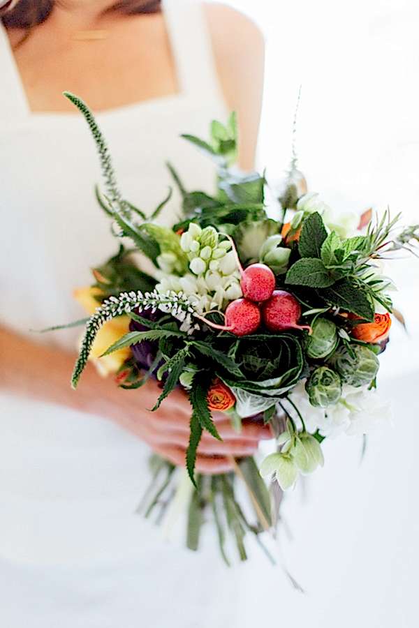 A woman in a white dress holds a veggie and flower bouquet to achieve a wedding without flowers