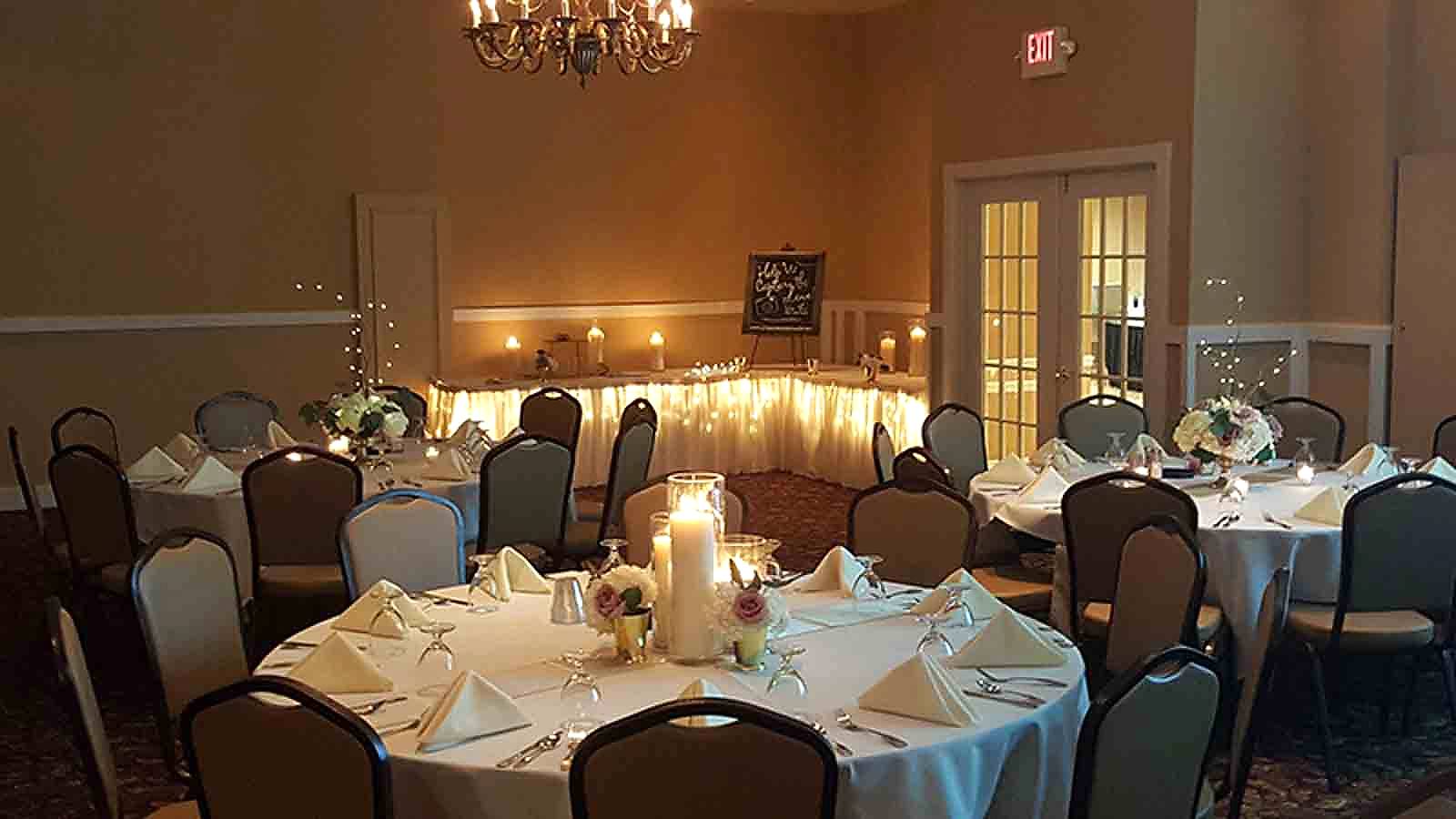 Brown and tan banquet chairs at a wedding reception around round set dinner tables, lit with candles, in an event room.