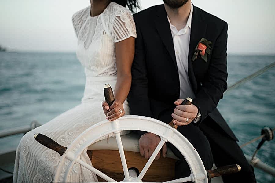 A couple in wedding clothes hold the wheel of a yacht on the water