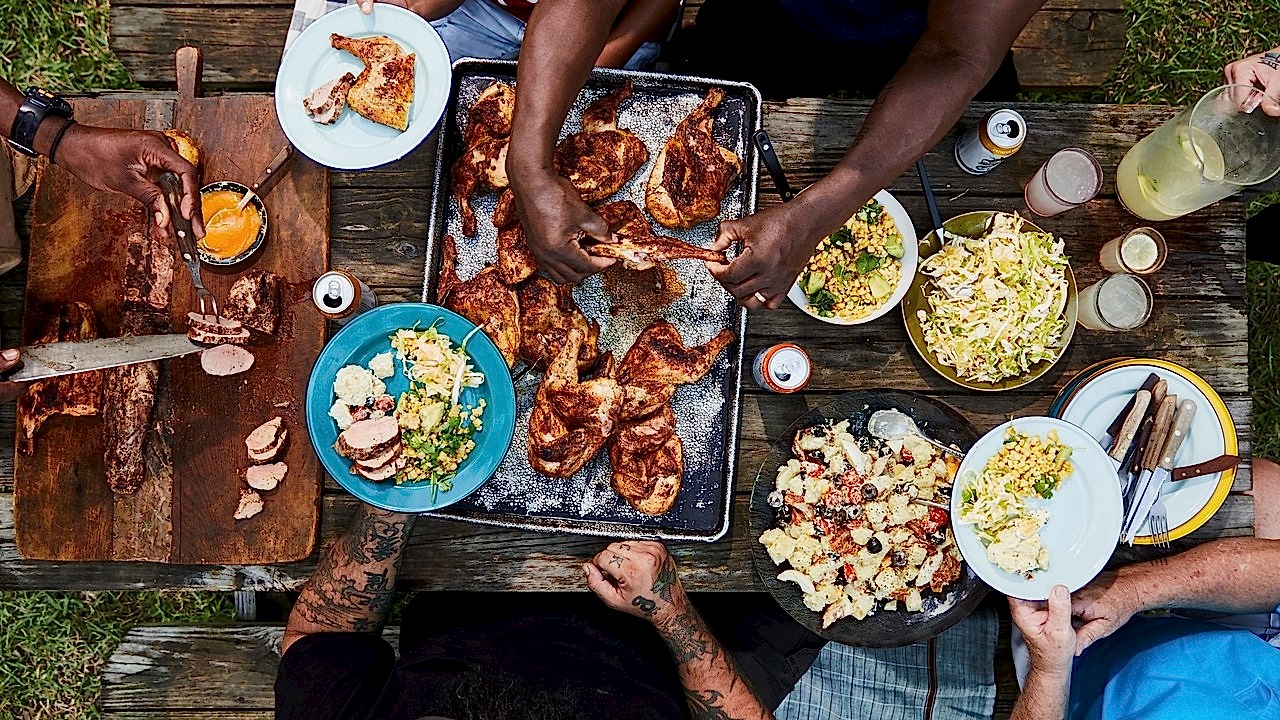 engagement party ideas for a cookout spread with chicken, corn salad, coleslaw, and more on a picnic table