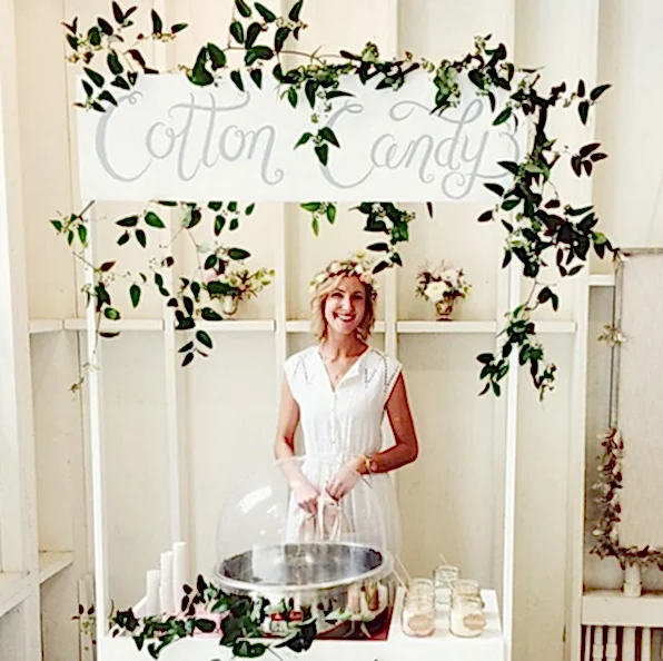 Woman in white manning a cotton candy station at an event as an engagement party idea