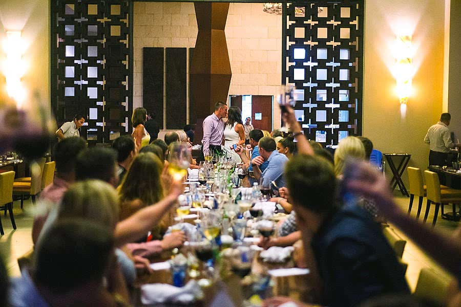 A couple kisses while standing at the head of a table as everyone at the party raises a glass in toast
