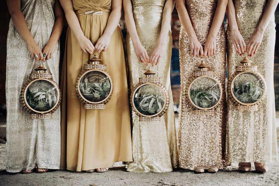 five women in shimmery metallic full-length dresses hold round copper lanterns filled with air plants for a wedding without flowers
