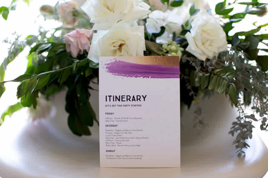 An Itinerary card leans against a pink and white flower arrangement