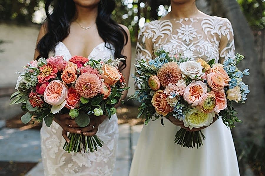 Two women wearing wedding dresses hold their bouquets