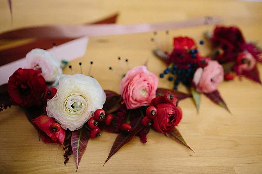 Pink, red, and white flower crowns with ribbons sit on a wooden table