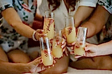 Womxn in matching pjs toast mimosas in stemless champagne glasses with their names written in gold calligraphy on them