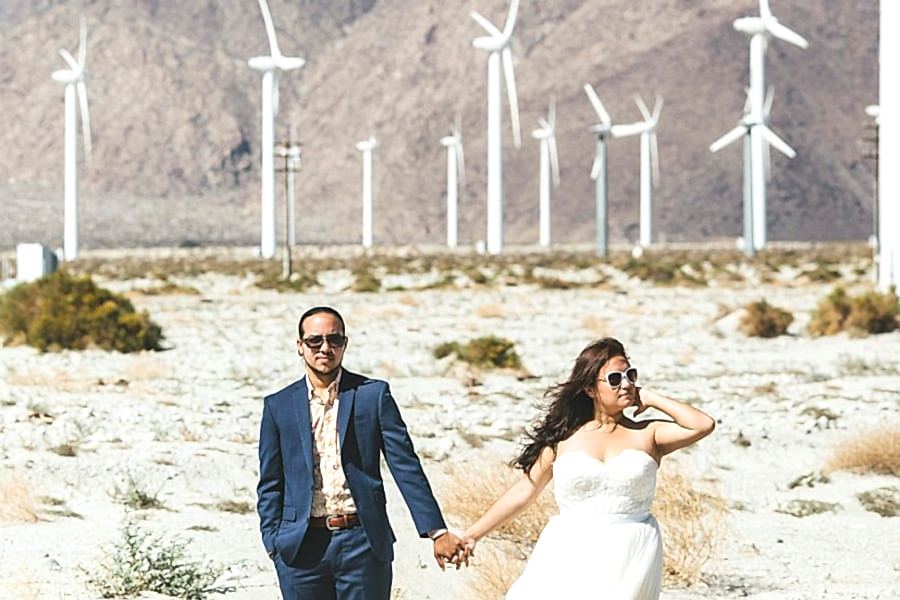 A wedding couple stands just outside a field of white windmills in the desert