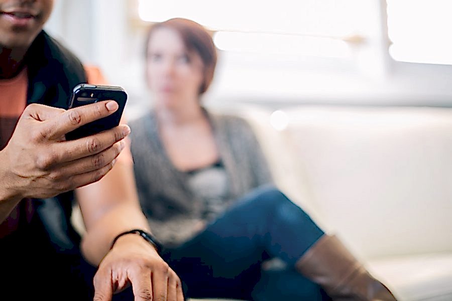 A man is texting someone while a woman looks at him texting someone
