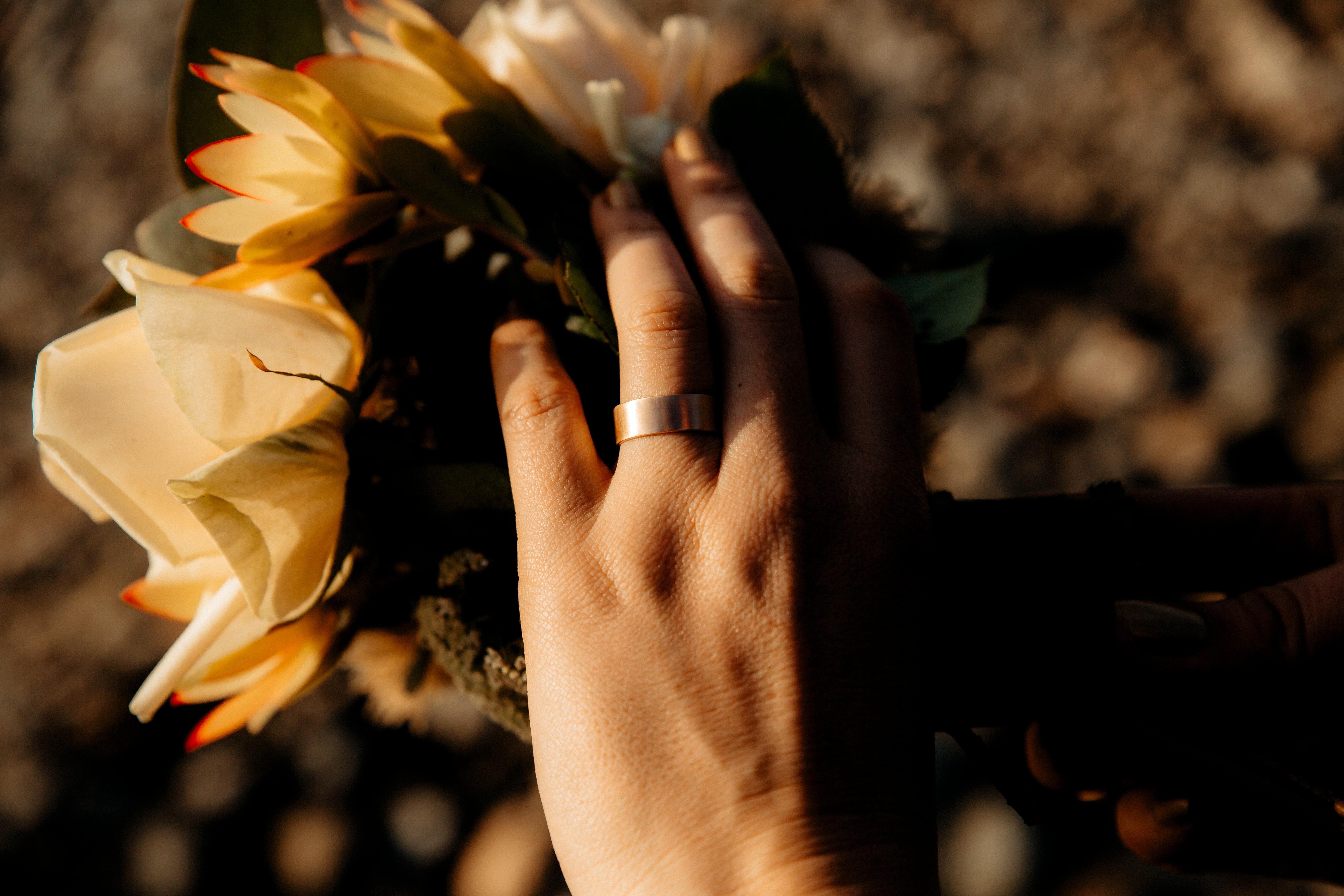 Closeup of a hand lightly touching a flower, wearing a Good Gold wedding band
