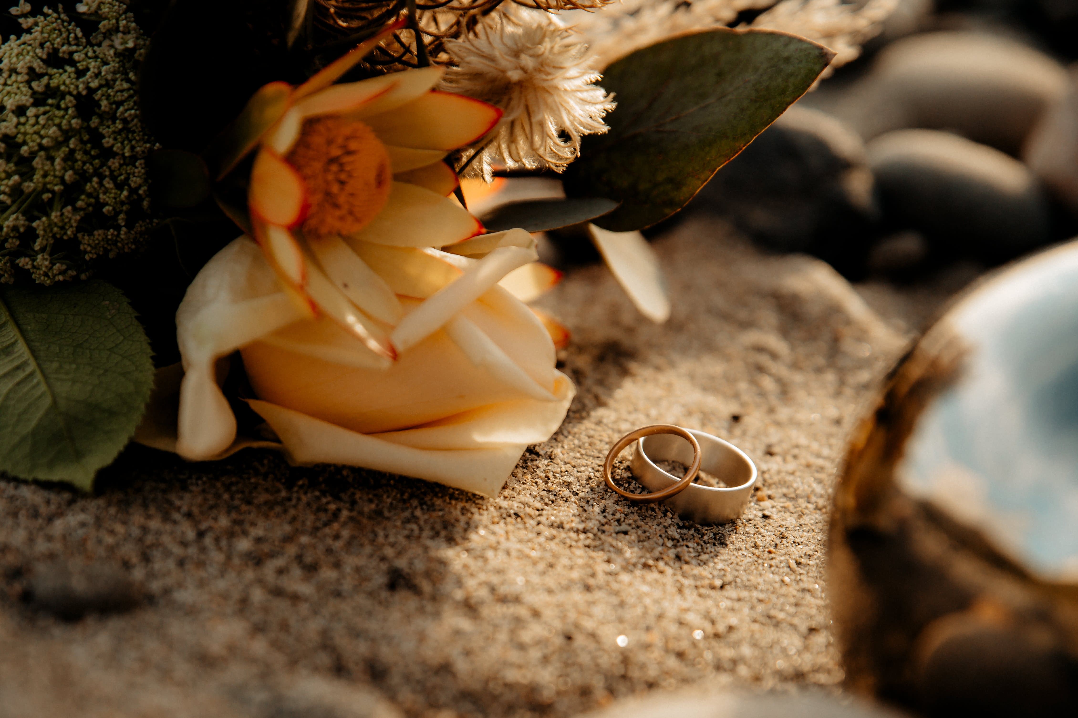 Two rings leaning against each other in the sand - Good Gold