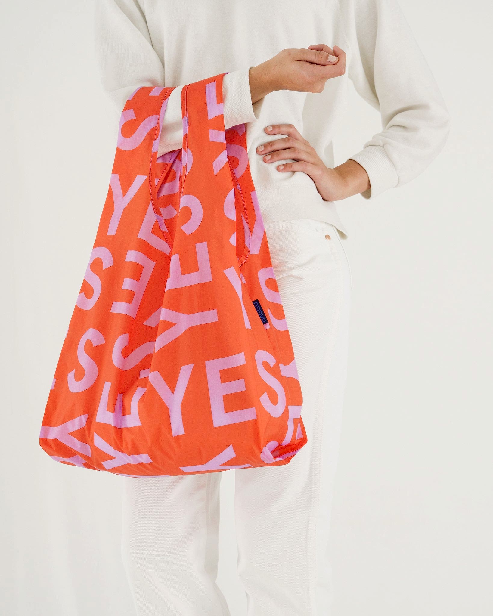 Woman in white holding reusable orange bag with the word YES on it for bridal shower favors