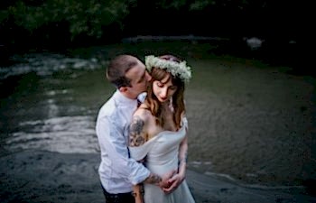 A wedding couple embrace while standing in a river