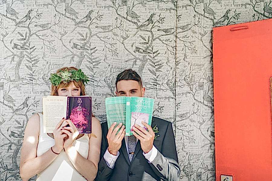 Two people hold books up to their faces, books with wedding readings in them.