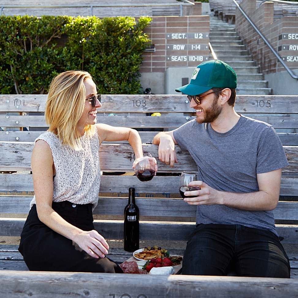 Two people sitting on a bench, happily enjoying some Winc wine