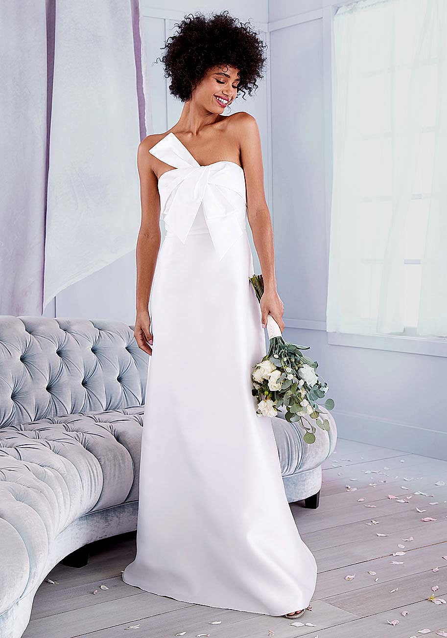 black woman with natural hair wearing a strapless white wedding dress smiling and holding a bouquet