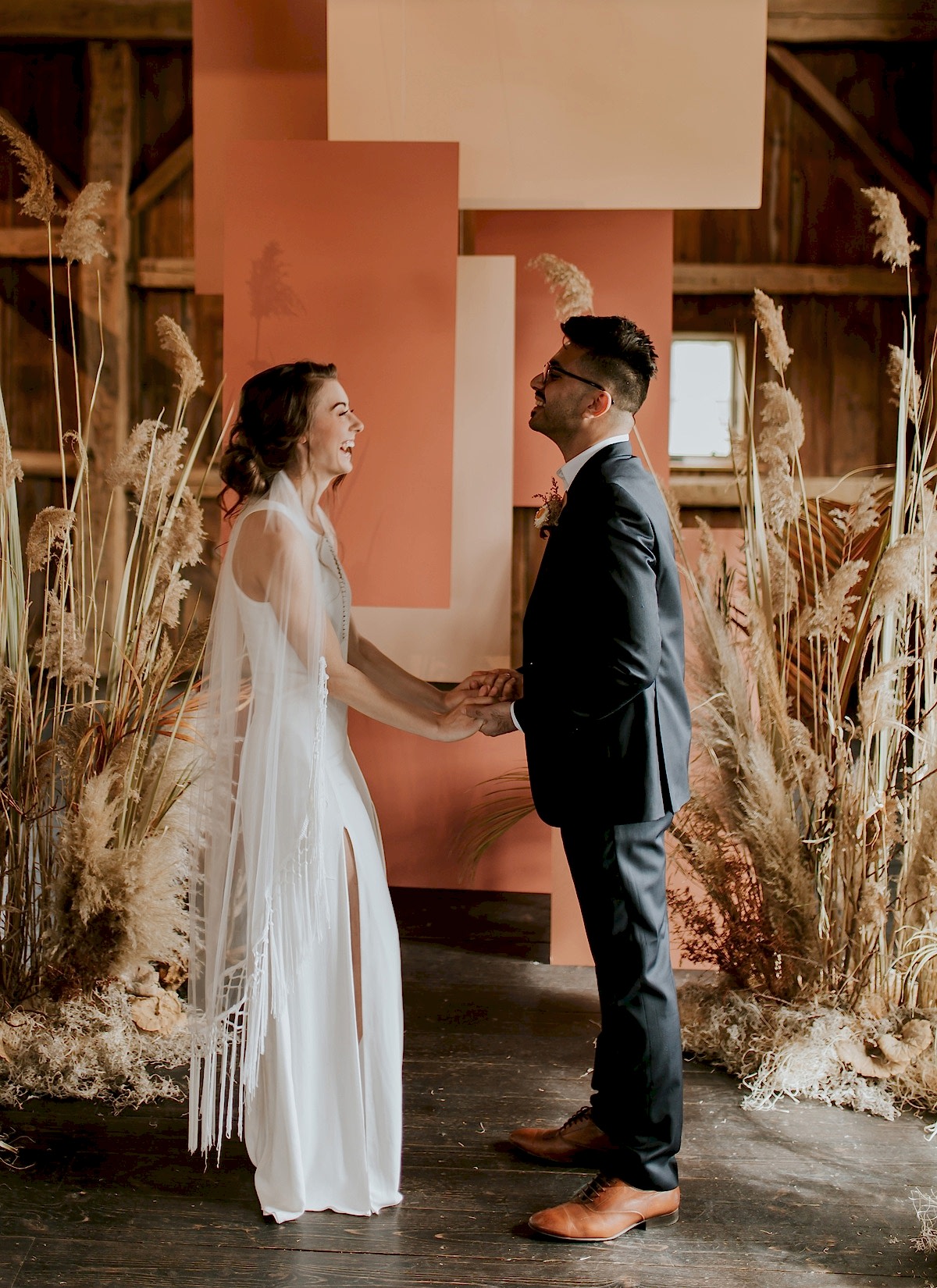 A wedding couple holds hands and smiles at each other.