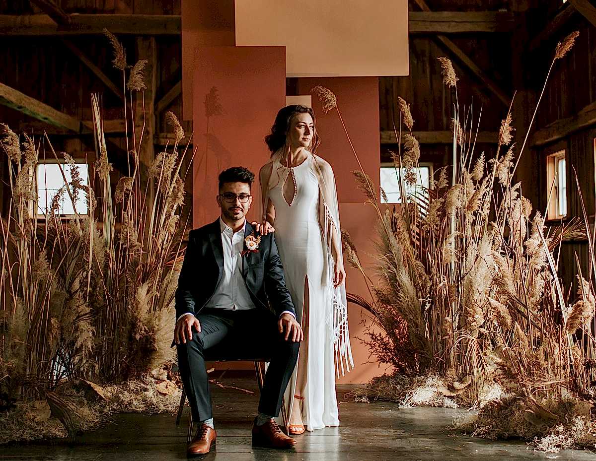A wedding couple pose in front of tall grass inside of a building.
