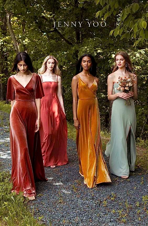 Four models walk down a path wearing dresses in fall wedding colors